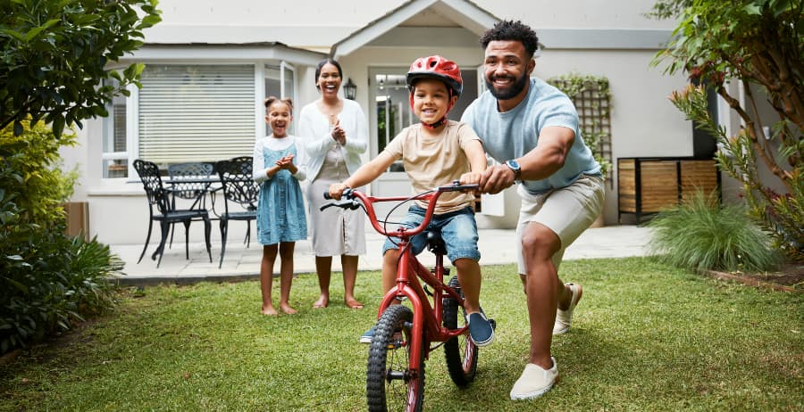Child learning to ride a bike in his backyard with family